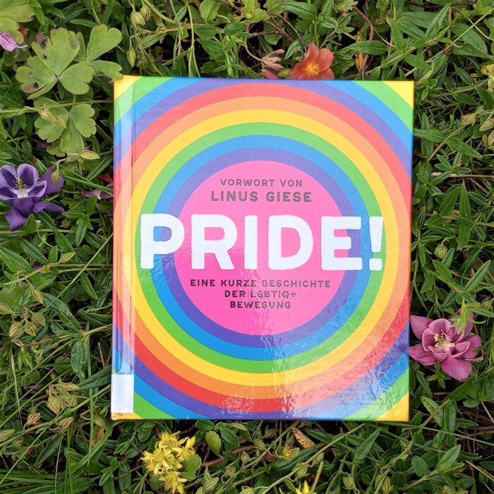 Ein Foto des Buchs "Pride" in einem Blumenbeet. Über das Foto führt ein Link zum Buch im Katalog der Stadtbücherei.