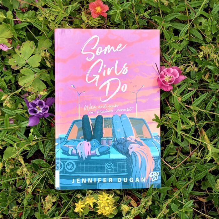 Ein Foto des Buchs "Some Girls do" in einem Blumenbeet. Über das Foto führt ein Link zum Buch im Katalog der Stadtbücherei.