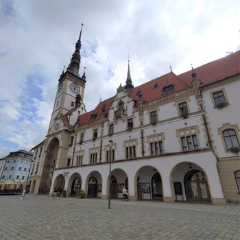 Ein Bild eines historischen Gebäudes in Olomouc. Es hat Bogengänge und einen Turm mit einer Turmuhr.