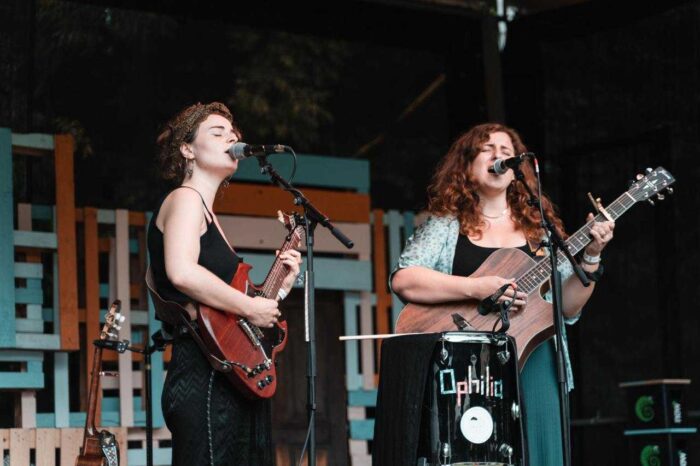 Ein Foto von zwei Frauen mit Gitarren, die in Mikros singen.