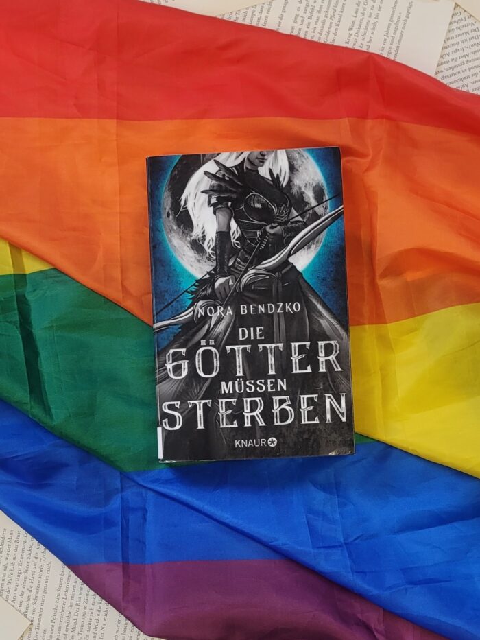 Das Buch "Die Götter müssen sterben" liegt auf einer Pride Flagge.