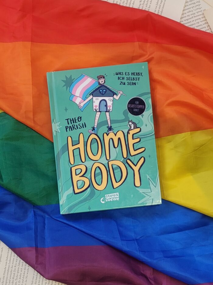 Das Buch "Home Body" liegt auf einer Pride Flagge.