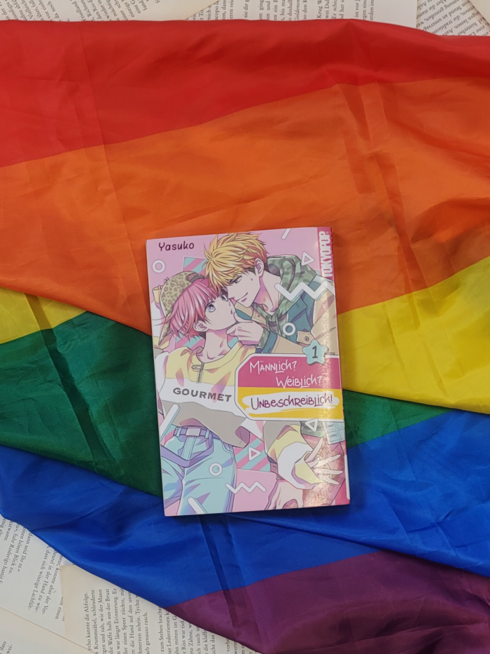 Das Buch "Männlich, weiblich, unbeschreiblich" liegt auf einer Pride Flagge.