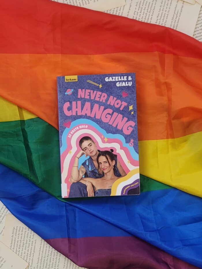 Das Buch "Never not changing" liegt auf einer Pride Flagge.