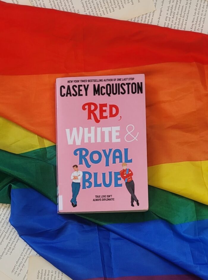 Das Buch "Red, white and royal blue" liegt auf einer Pride Flagge.