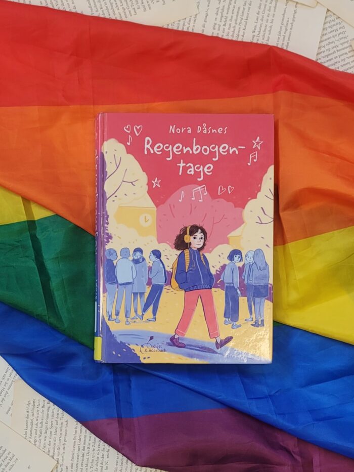 Das Buch "Regenbogentage" liegt auf einer Pride Flagge.