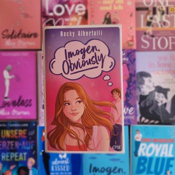 Buchtipp: Imogen, obviously Das Buch "Imogen, Obviously" liegt auf einem Hintergrund aus bunten Büchern, die die bisexuelle Pride-Flagge bilden.