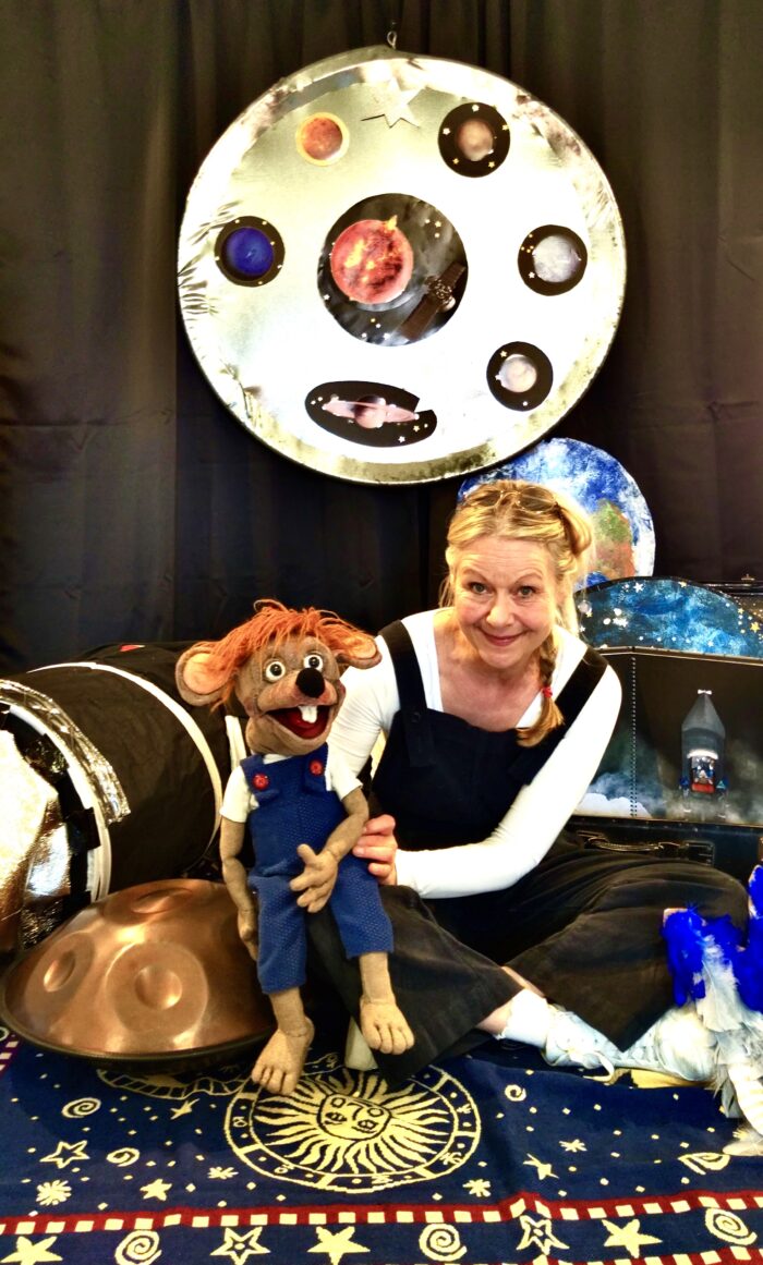 Hilda Gardner sitzt mit einer Puppe vor ihrem Bühnenbild.