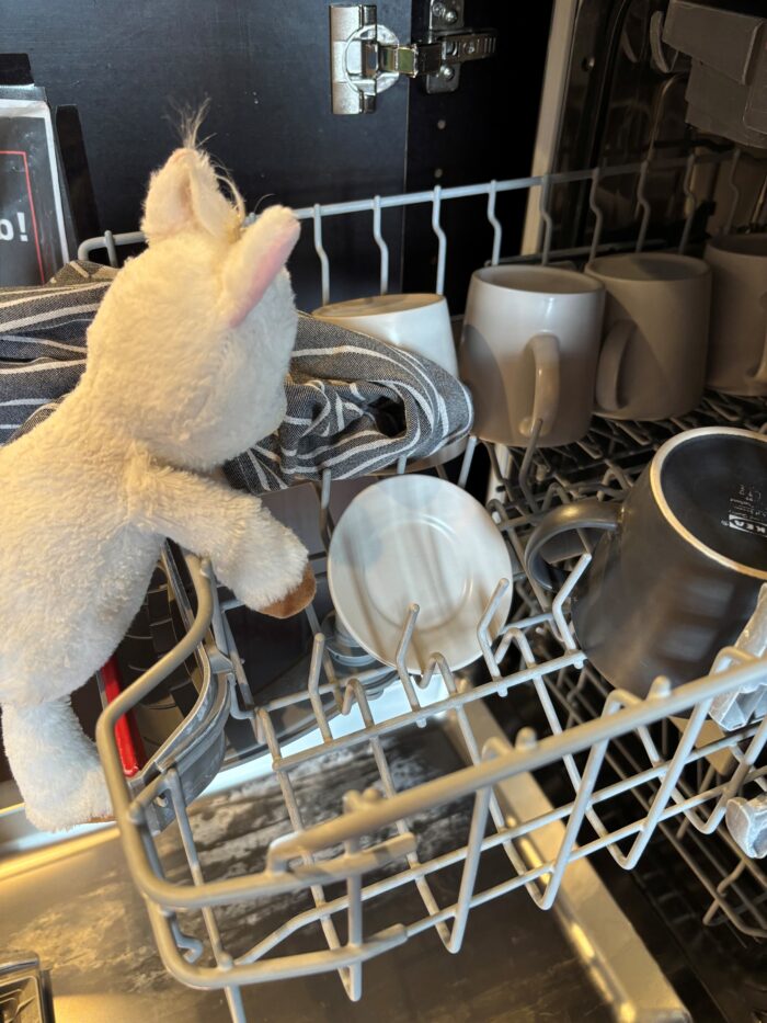 Finchen das Plüsch-Alpaka räumt die Geschirrspülmaschine aus.