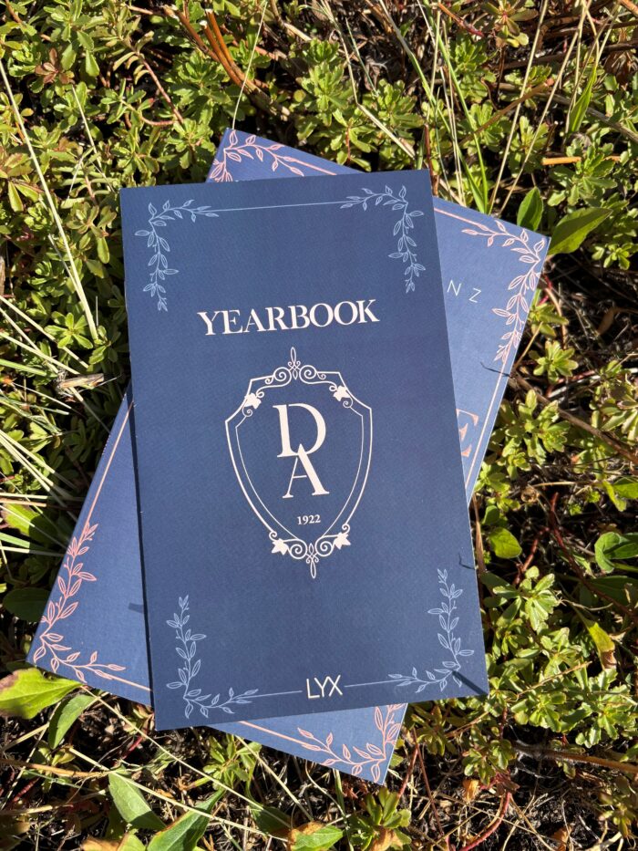 Der vierte Teil der Dunbridge Academy Reihe liegt im Gras. Darüber liegt das Yearbook, welches in der Erstauflage des Buches mitgeliefert wurde.