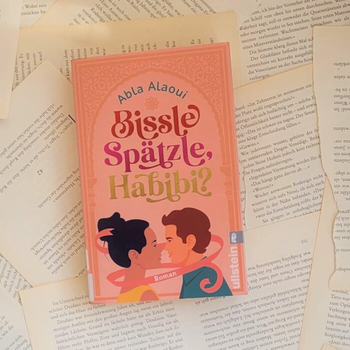 Das Buch "Bissle Spätzle, Habibi?" von Abla Alaoui liegt auf einem Hintergrund aus Buchseiten