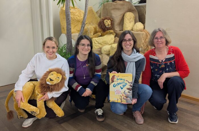 Vier Mitarbeiterinnen der Stadtbücherei stehen vor der Savannen-Dekoration der Kindergartenaktion. Eine Frau hält einen Plüschlöwen und eine Frau das Buch "Genug gebrüllt, Löwe":