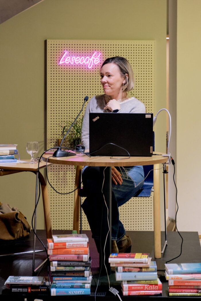 Zu sehen ist Referentin Isabel Fraas auf der Bühne. Zu ihren Füßen liegen die Bücher der Saison.