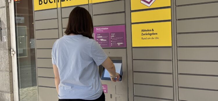 Eröffnung der Büchereistation in Heidingsfeld: Rückgabe und Vorbestellungen abholen rund um die Uhr Zu sehen ist eine junge Frau, die vor der Büchereistation in Heidingsfeld steht und diese bedient.