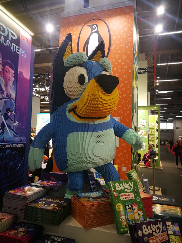 Bluey, ein Hund aus einer Zeichentrickserie aus Legosteinen gebaut. Vor ihm sind die passenden Bluey Bücher drapiert.